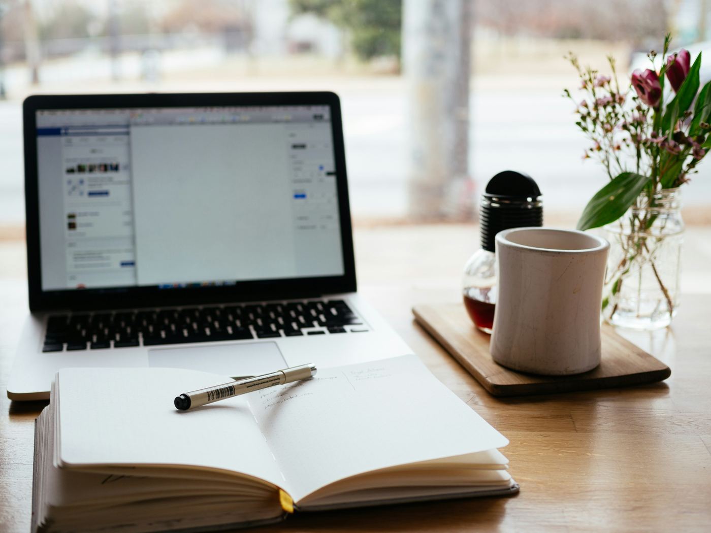 An open notebook and pen next to a laptop on a desk